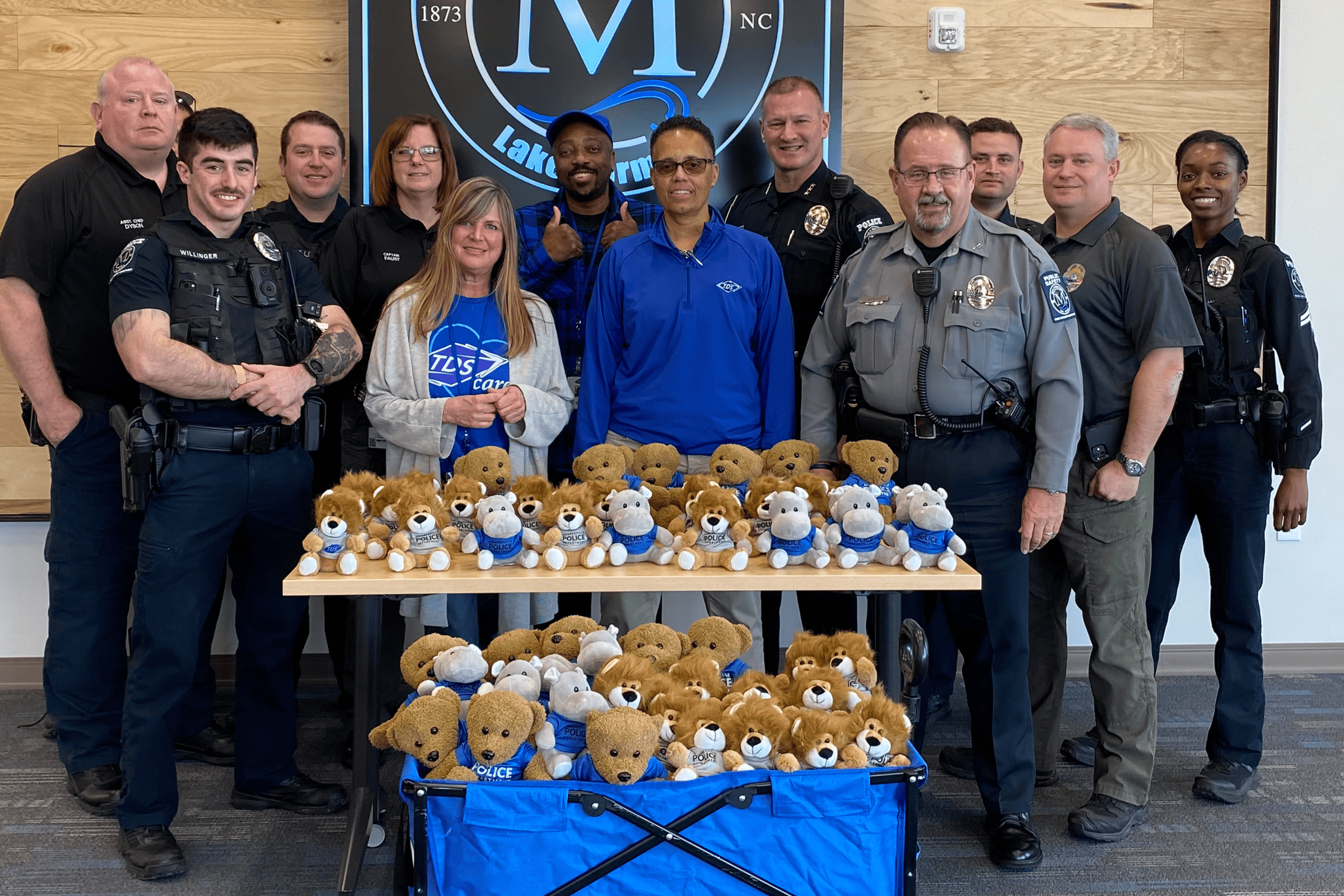 Mooresville PD with TDS workers in behind a table that is lined with stuffed bear toys.