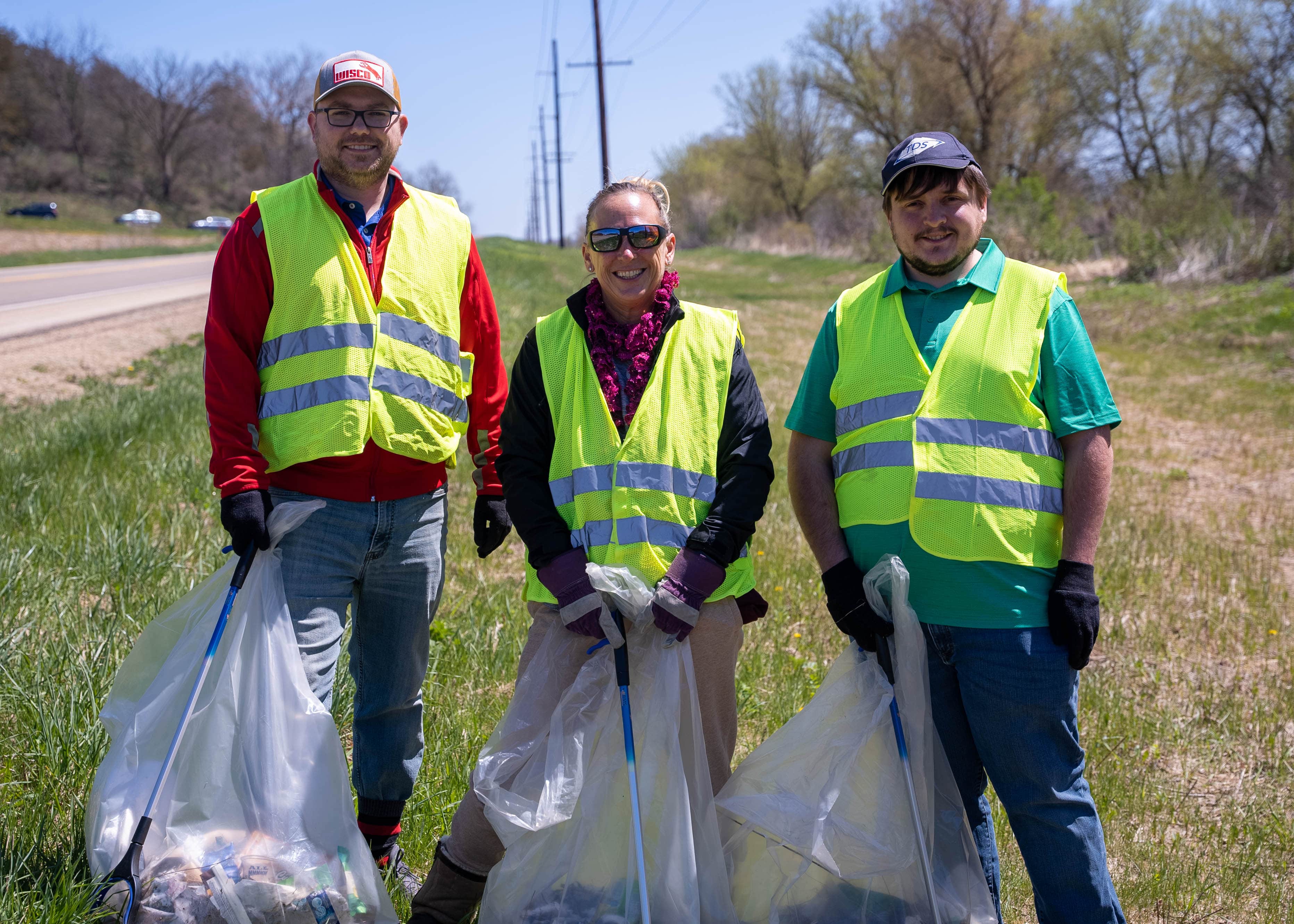 Two men and one woman wearing reflective vests doing highway trash pickup