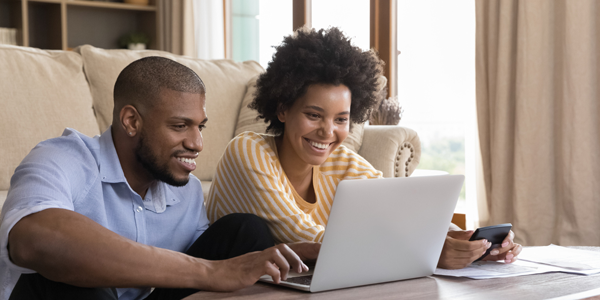 Young black couple sitting on the floor of their living room at their coffee table on a laptop and cell phone