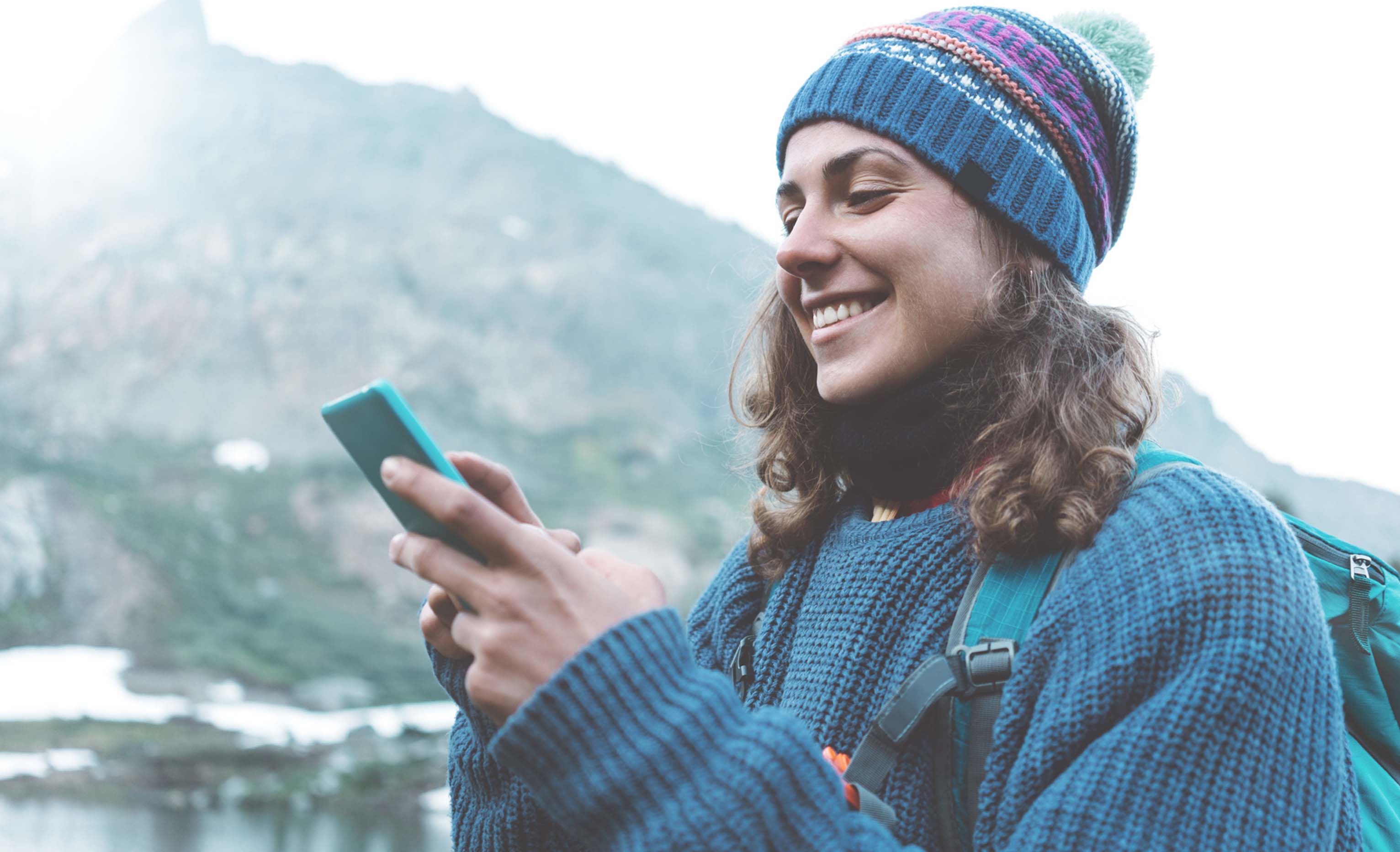 Woman smiling while using her mobile phone outside in cold weather.