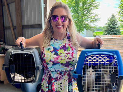 Women in colorful dress holding pet carrier in both hands.