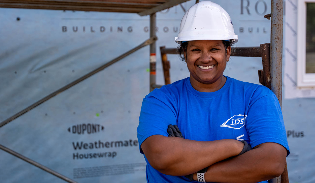 Worker smiling at the camera wearing a hard hat in front of a construction site.