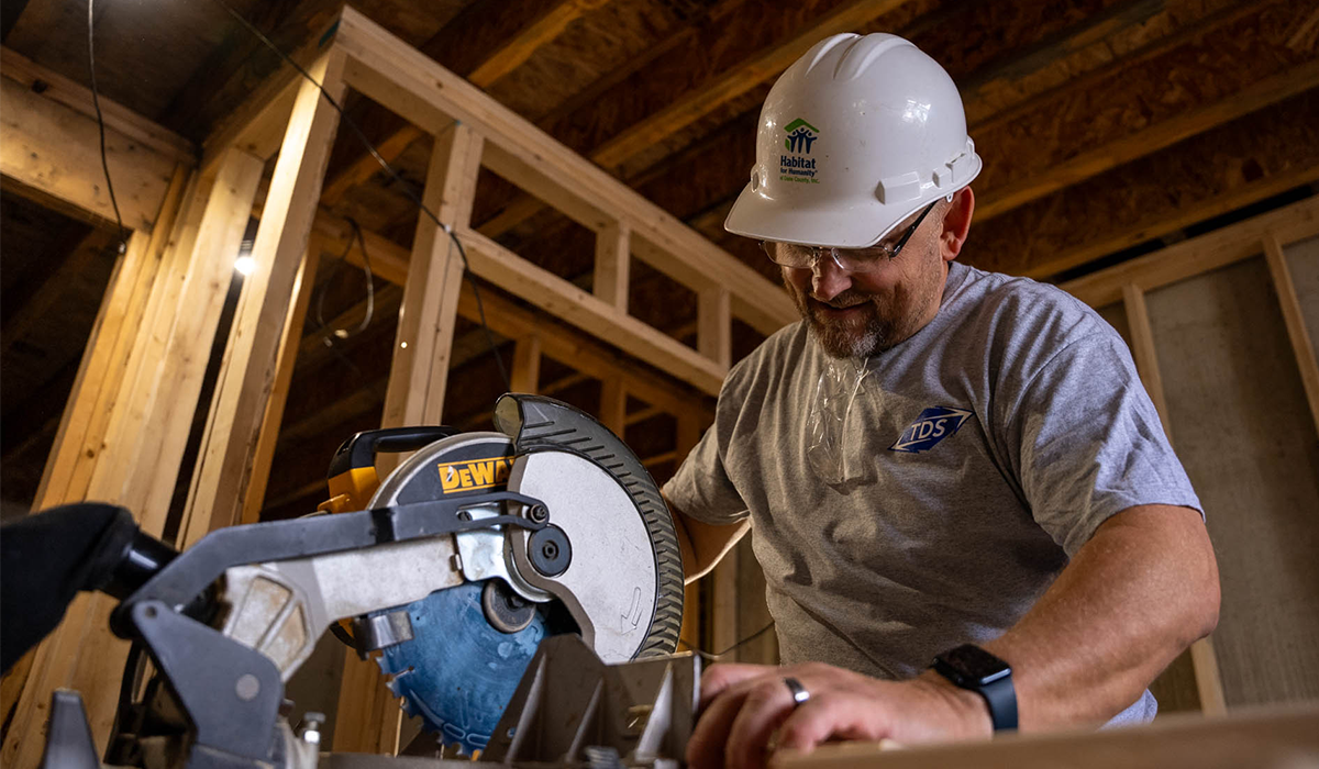Worker wearing a hard hat using a saw to cut wood on construction site