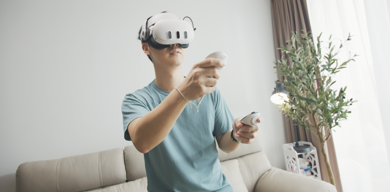 Boy in green shirt wearing a virtual reality headset holding a controlller in each hand