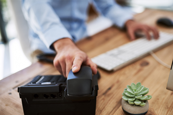 Man at home desk hanging up landline phone